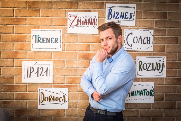 Iwo Konopek stojący przed ceglaną ścianą hasła Trener, zmiana, biznes, coach, rozwój, doradca, IP 121
